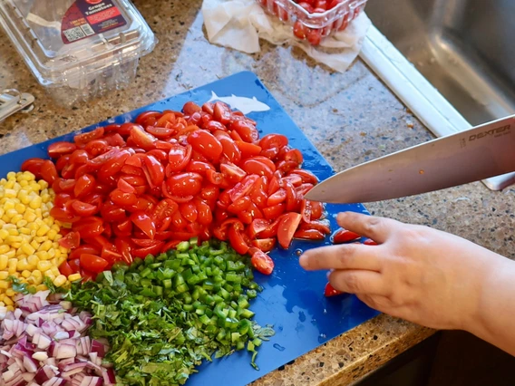 Tomatoes, corn, onion and bell pepper chopped on cutting board