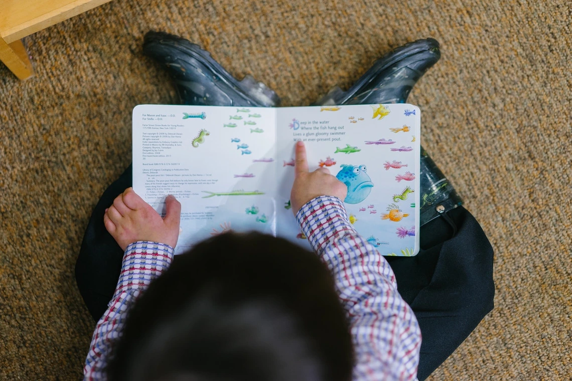 Young child reading book and pointing to fish on pages.