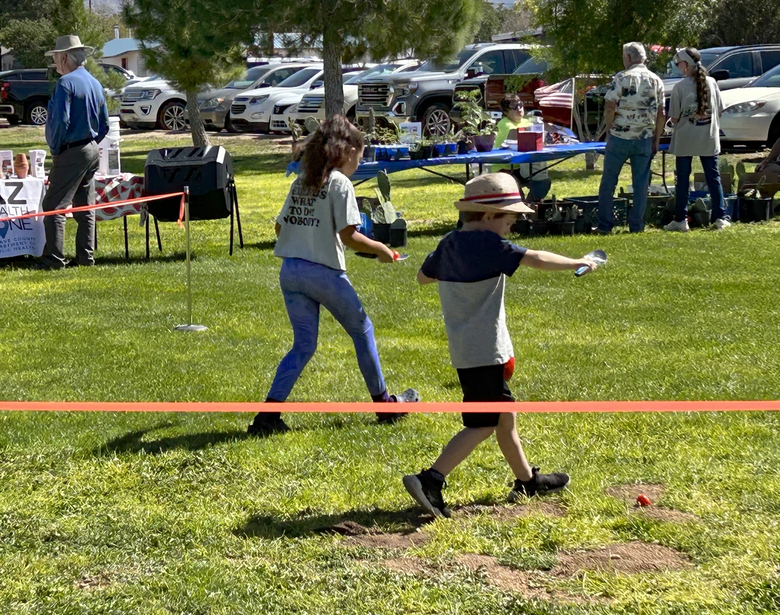 Two kids in grass walking fast with small shovels and racing