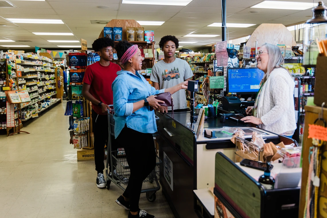 mother and teen boys paying for food at a small grocery store checkout