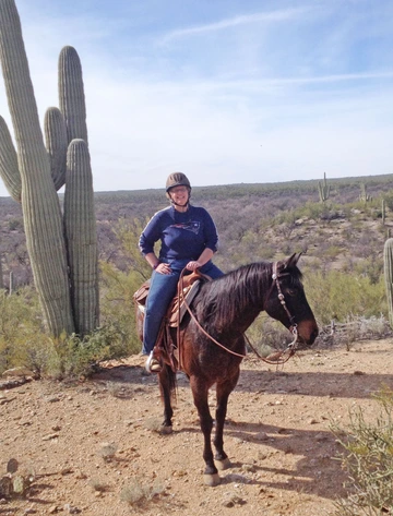 Woman on horse in western tack standing in front of a Saguaro cactus