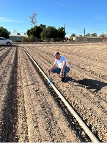 man kneeling in filed next to long pipe in crop row that has irrigation sprinkler head at spaced intervals