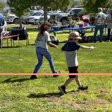 Two kids in grass walking fast with small shovels and racing